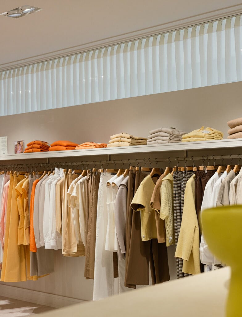 Kledingwinkel met diverse kledingstukken en accessoires in neutrale kleuren.
