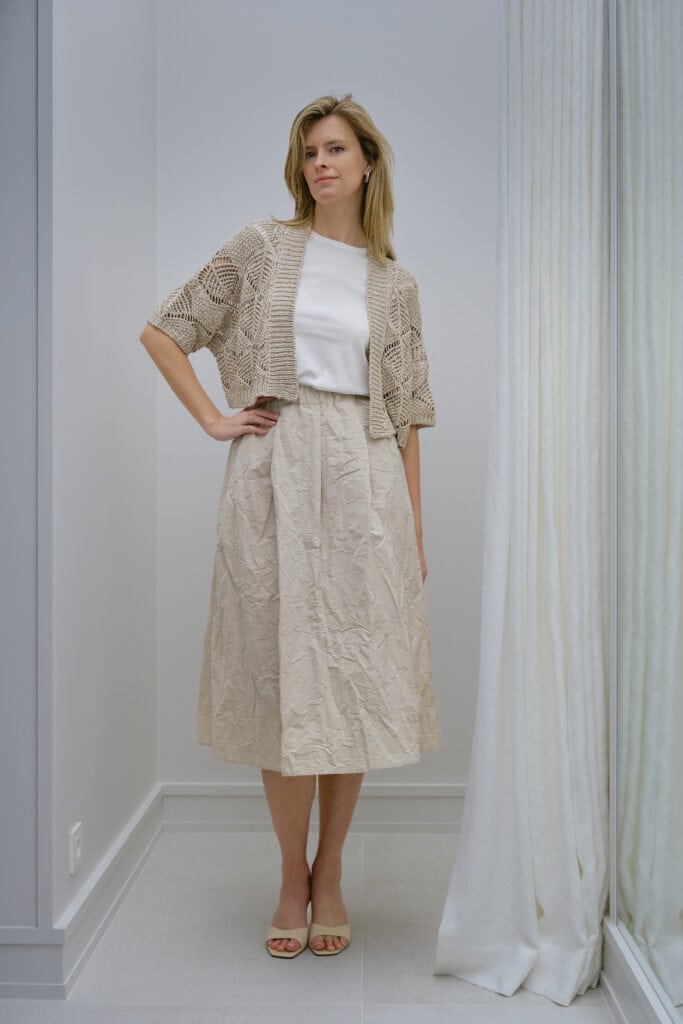 Vrouw in beige zomerjurk en kanten cardigan in lichte kamer.