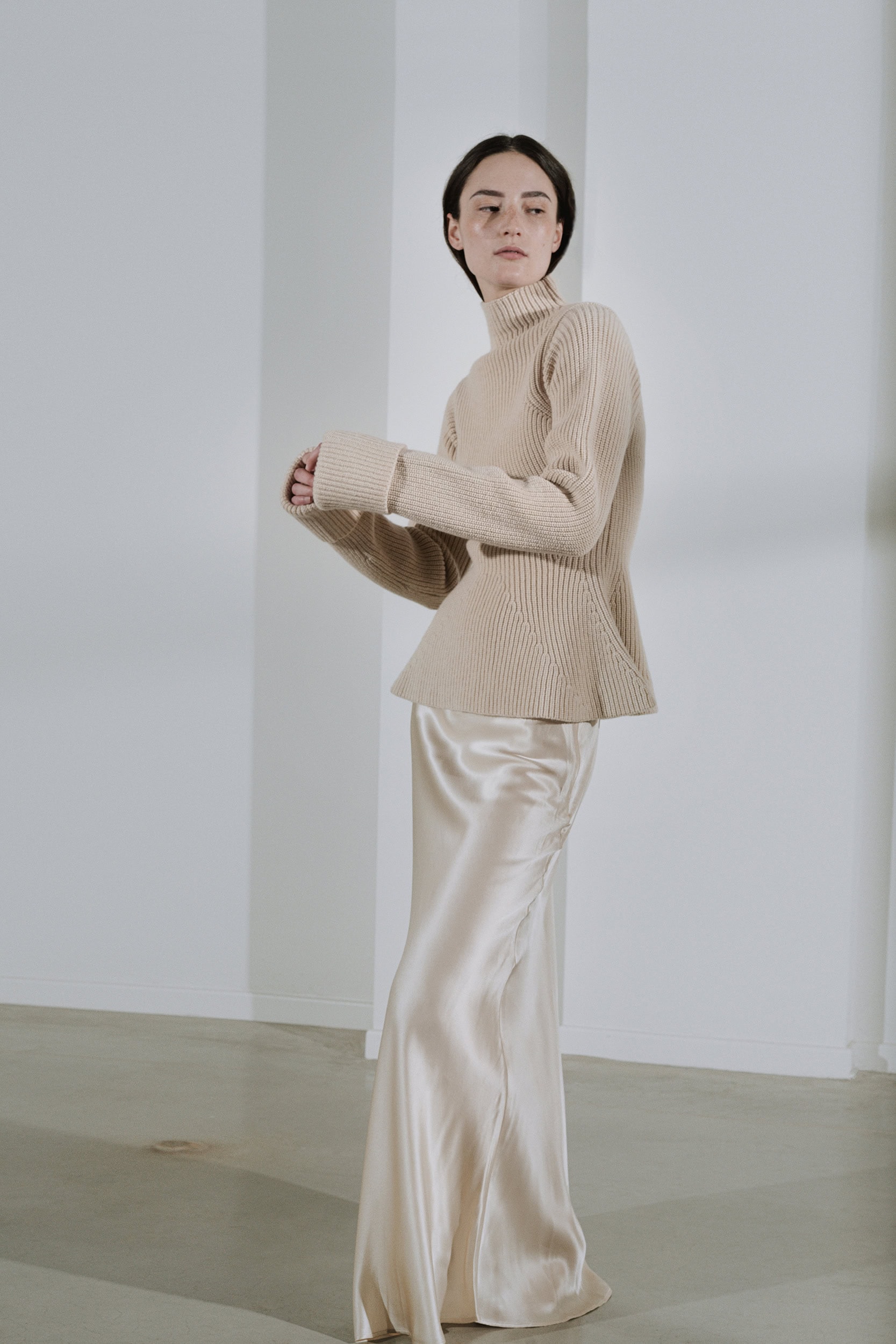 Modieuze vrouw in beige sweater en satijnen broek bij Sirocco.