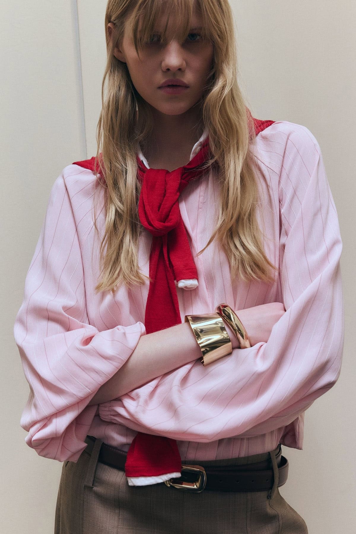 Modieuze vrouw in roze blouse met rode sjaal en gouden accessoires.