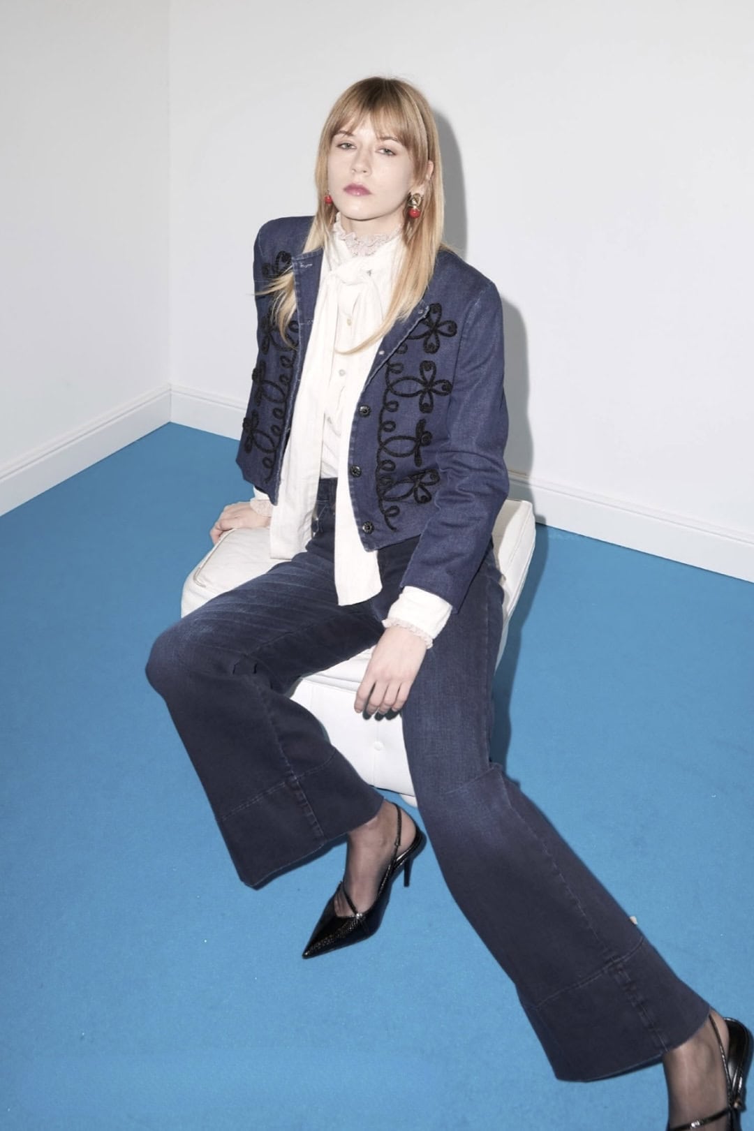 Modieuze vrouw in denim outfit zittend op witte stoel.