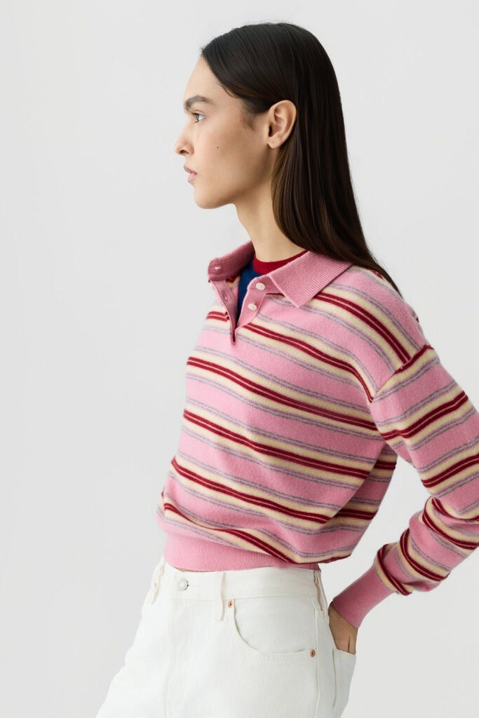 Damesmodel in roze gestreepte polo met witte broek, zijaanzicht.